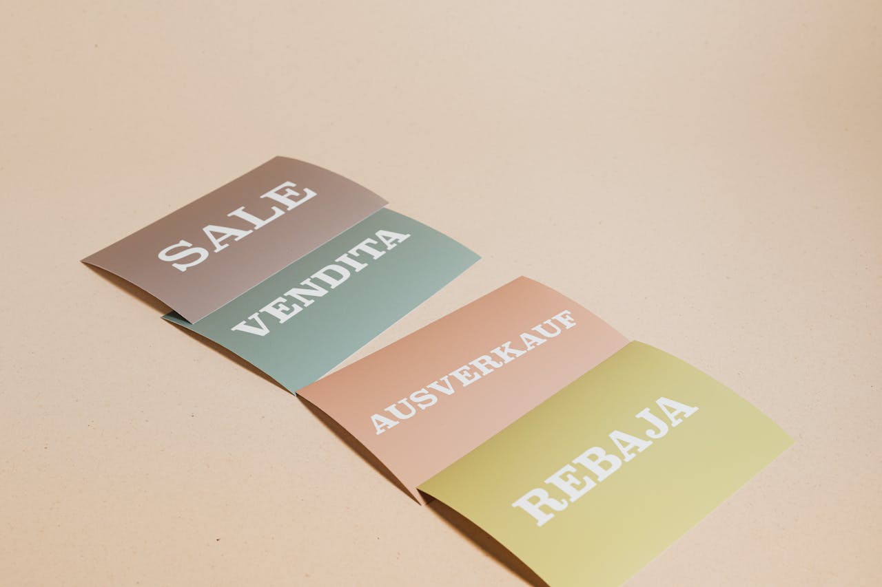 cta-bg Four sale signs in different languages on a beige background, ideal for retail promotions.